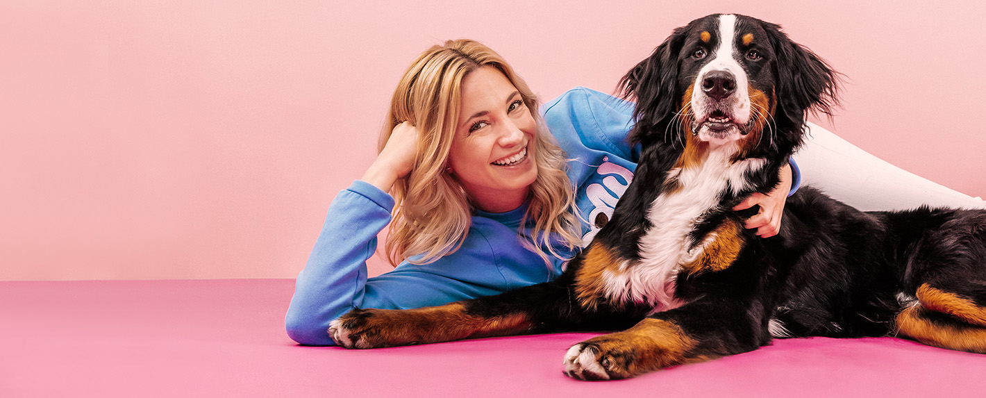 Katharina Miklauz tumbada con un perro de montaña bernés en un suelo rosa frente a una pared rosa