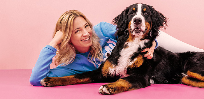 Katharina Miklauz tumbada con un perro de montaña bernés en un suelo rosa frente a una pared rosa