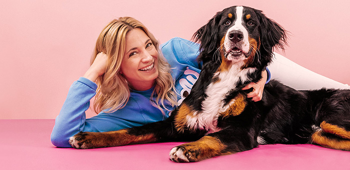 Katharina Miklauz sdraiata con un cane da montagna bernese su un pavimento rosa davanti a un muro rosa